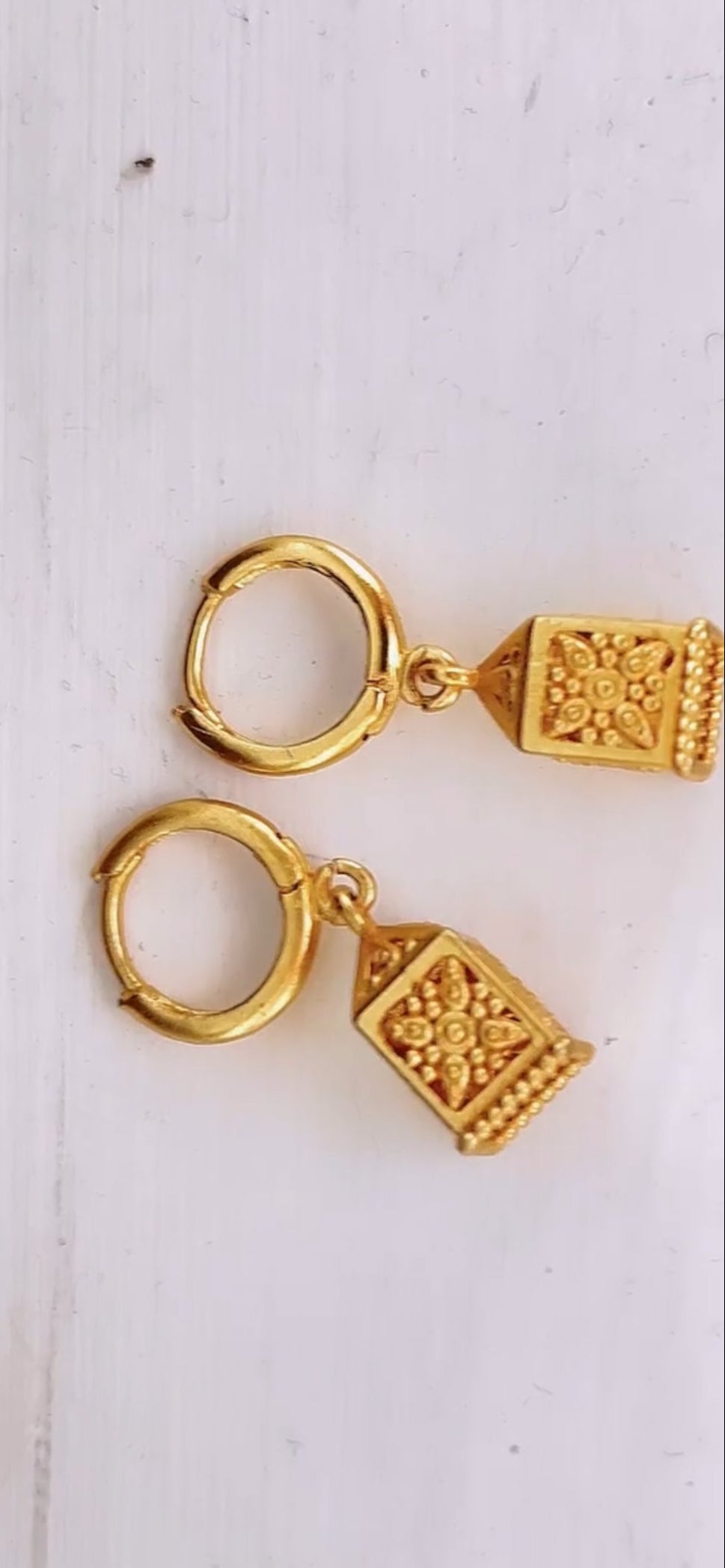 Gold hoop earrings with square designs on a white background