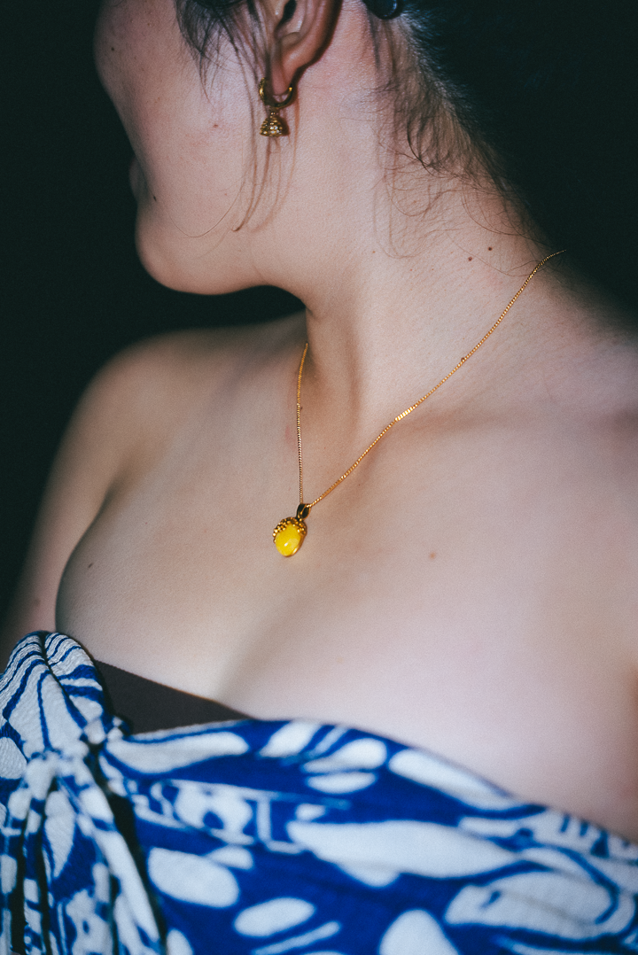 Close-up of a person wearing a gold necklace with a yellow pendant against a dark background.