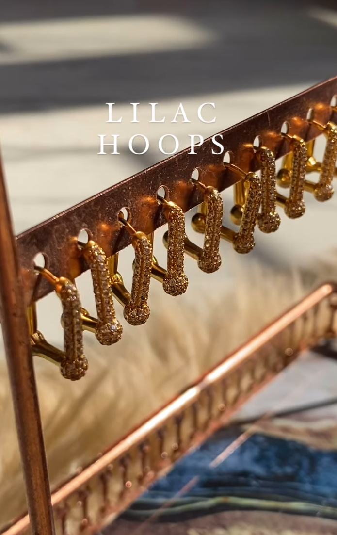 A pair of lilac-colored hoop earrings displayed on a stand, with the brand name 'Lilac Hoops' visible at the top.