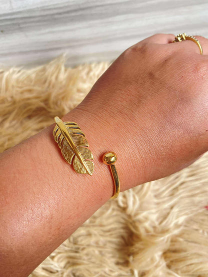 Gold feather bracelet on a wrist with a neutral background