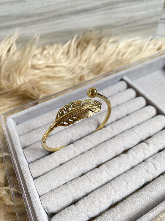 Gold feather-shaped bracelet on a gray jewelry tray with feathers in the background