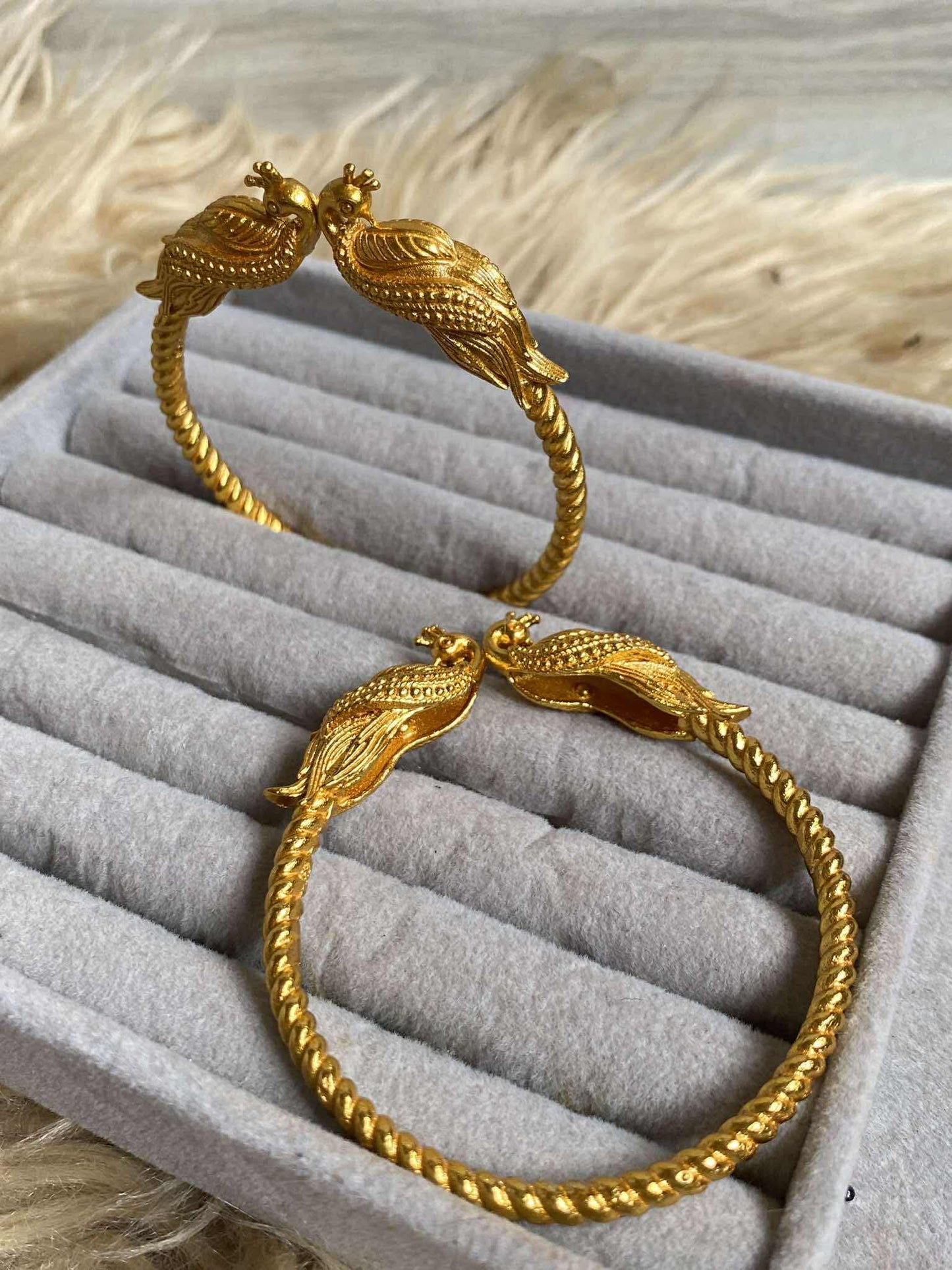 Gold polished bracelet with peacock design on a gray jewelry display