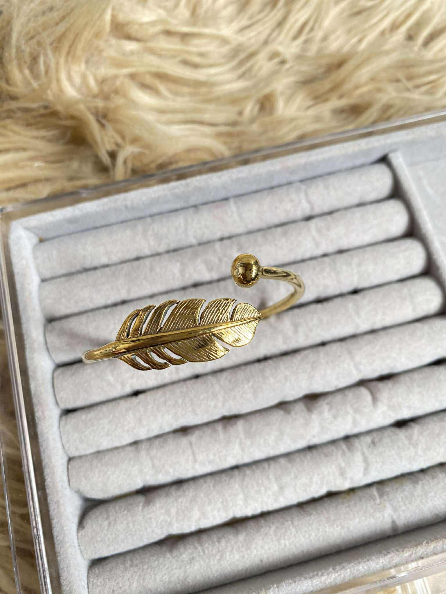 Gold feather-shaped earring in a jewelry box with a fur background
