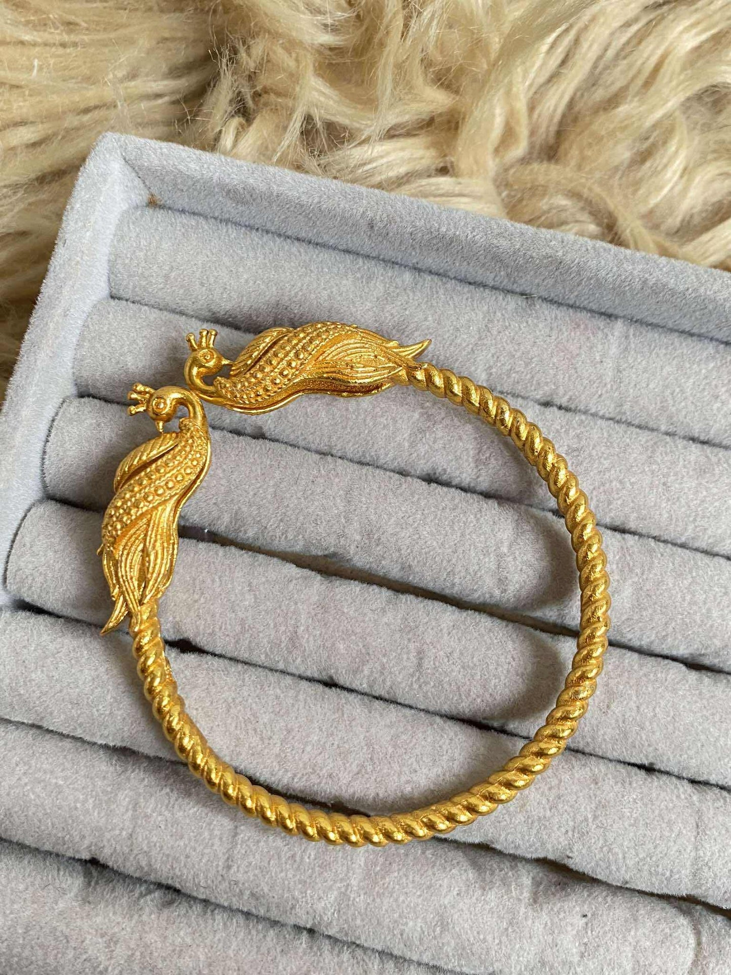 Gold bracelet with peacock design on a gray surface