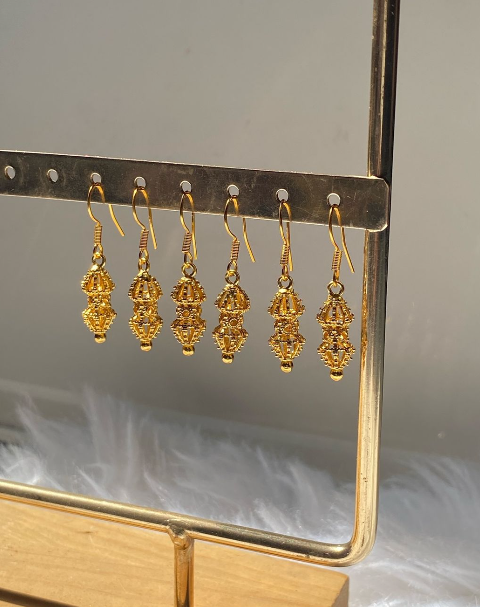 A pair of gold-colored hoop earrings with intricate designs displayed on a stand.