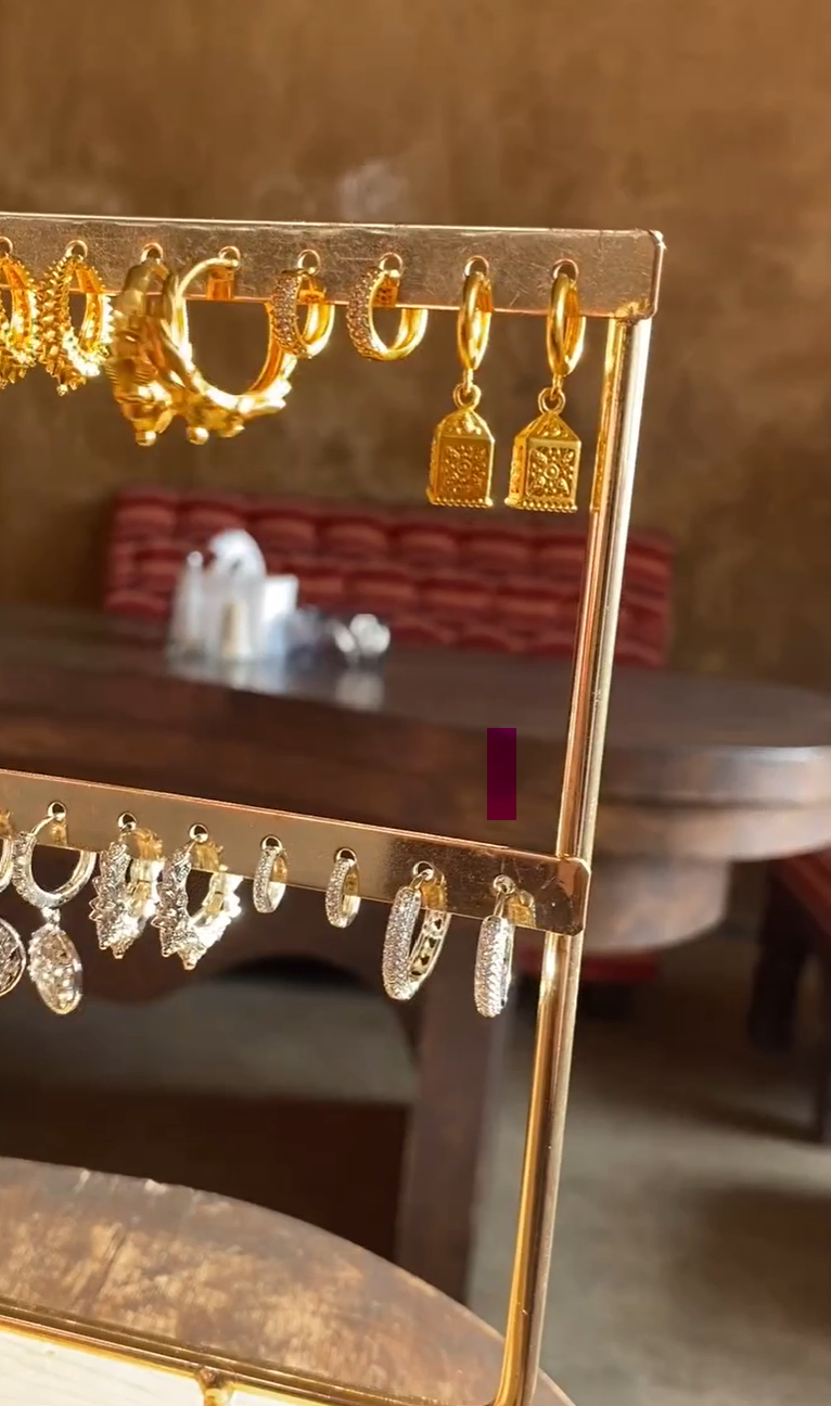 Gold earring display rack with lantern earrings on a blurred background