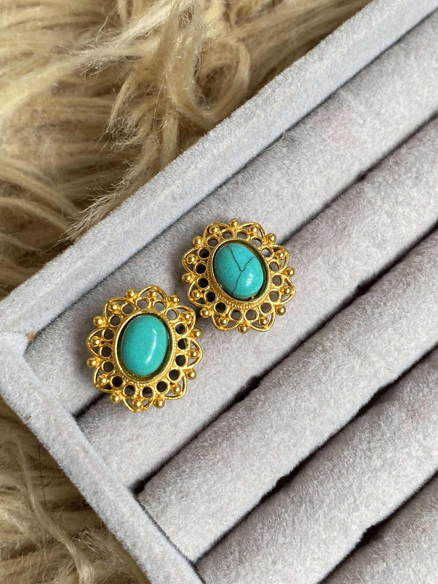Turquoise earrings with gold frames on a gray surface