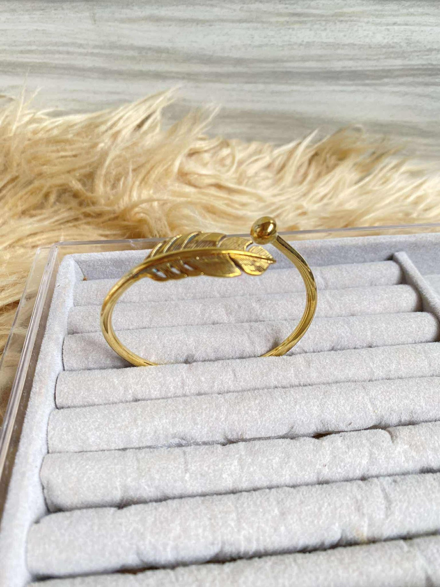 Gold bracelet on a white jewelry display with dried grass in the background