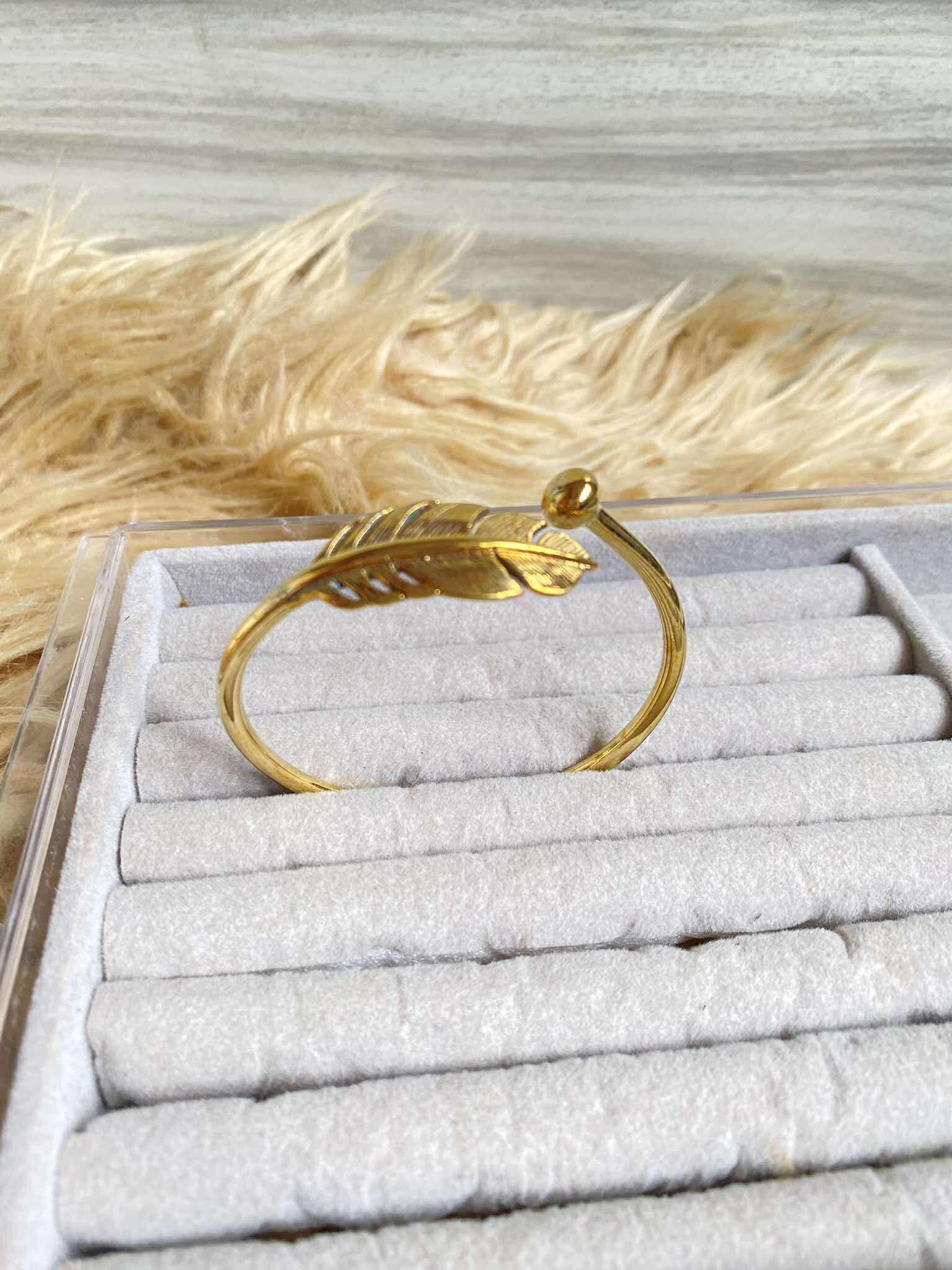 Gold bracelet on a white jewelry display with dried grass in the background