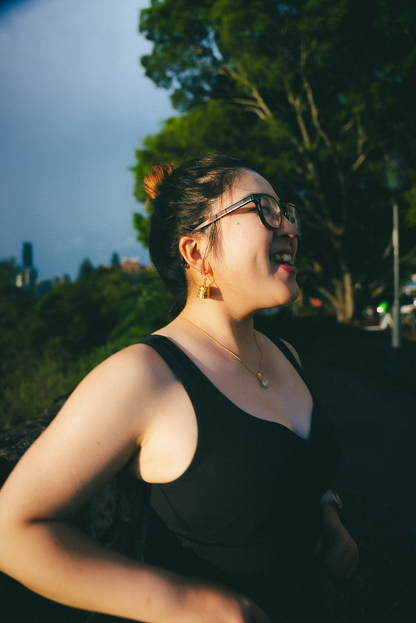 Woman wearing Kala:Cha Earrings and a black top outdoors with trees in the background