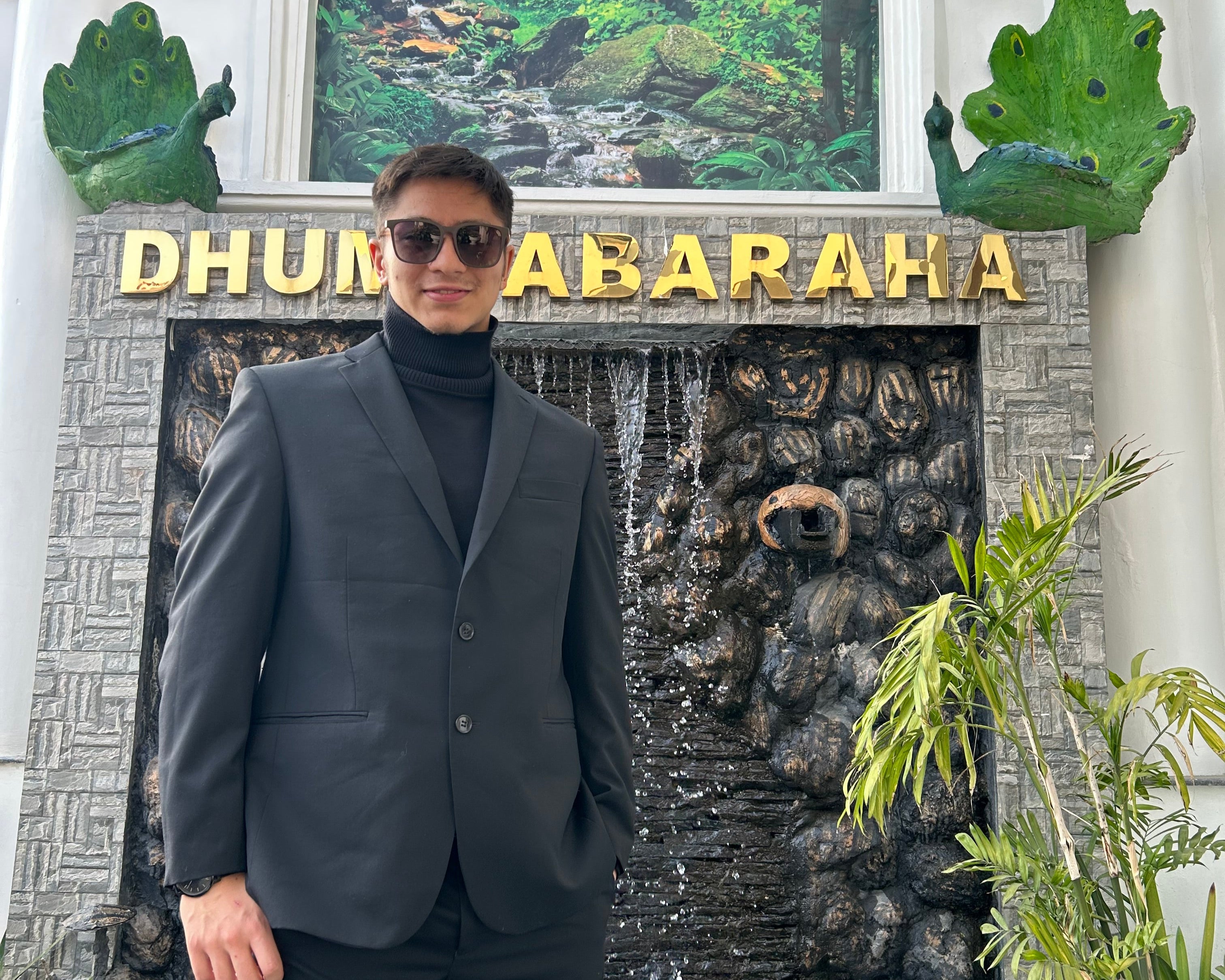 Person standing in front of a decorative entrance with plants and a sign.