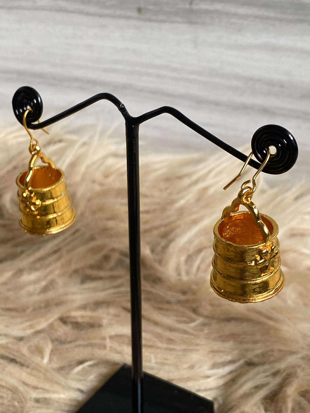 Kala:Cha Earrings on a black stand with a textured beige background