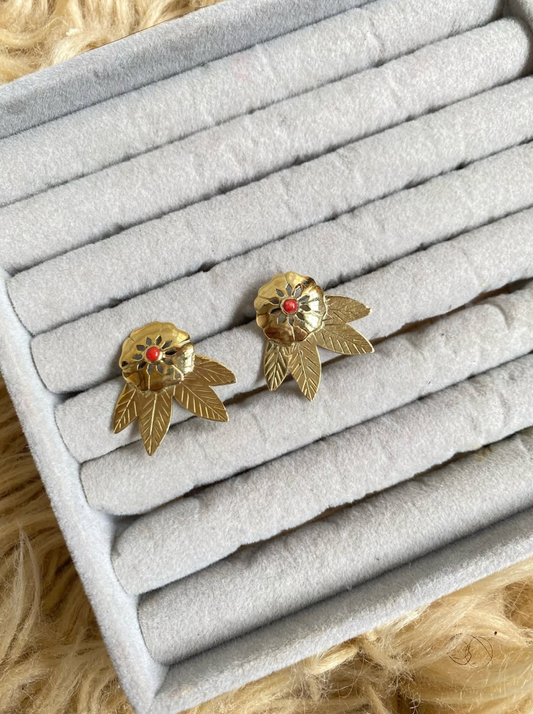 Gold leaf-shaped earrings with red centers on a gray jewelry tray.