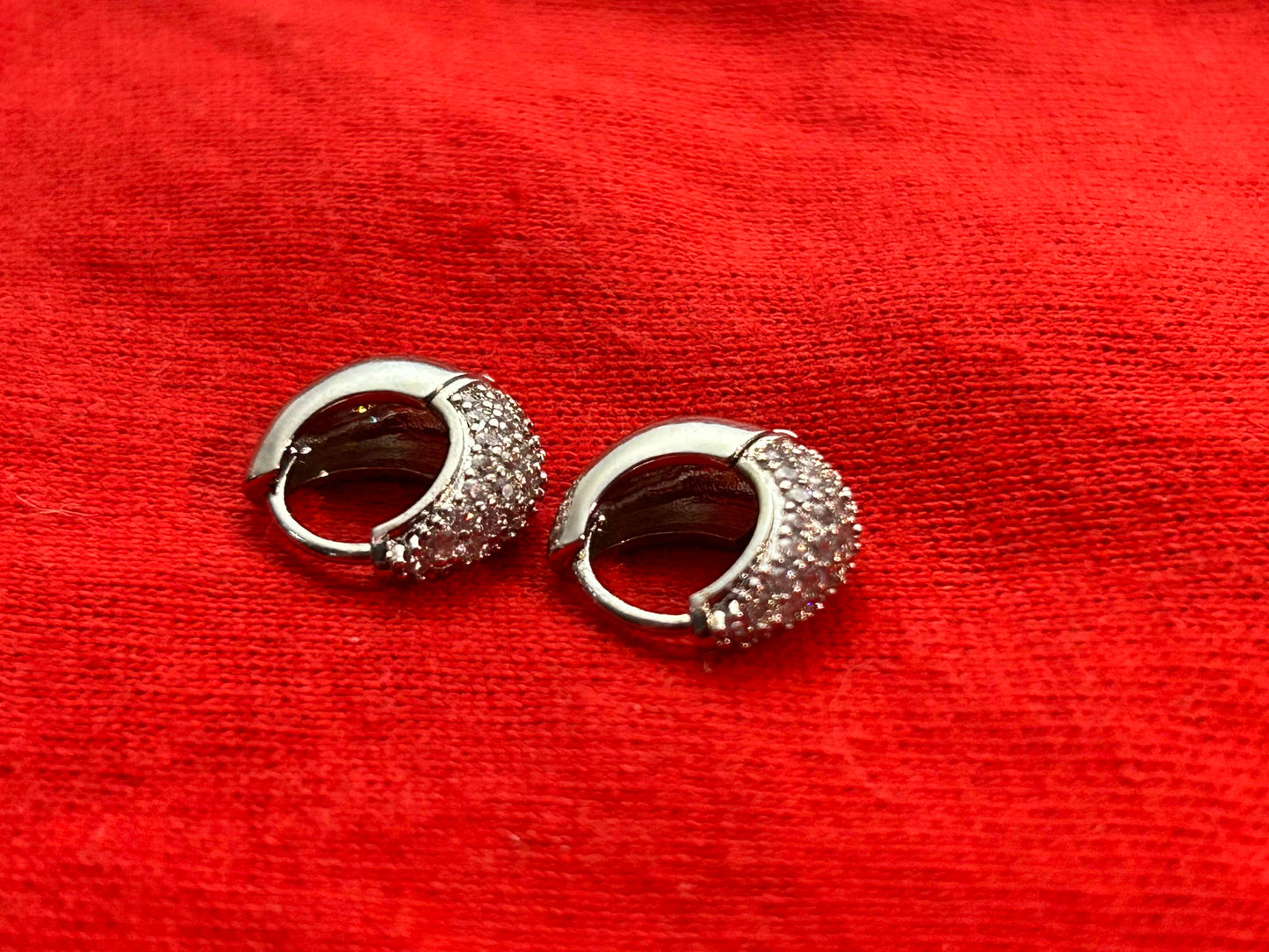 A pair of silver droplet hoop earrings placed on a red textured surface.